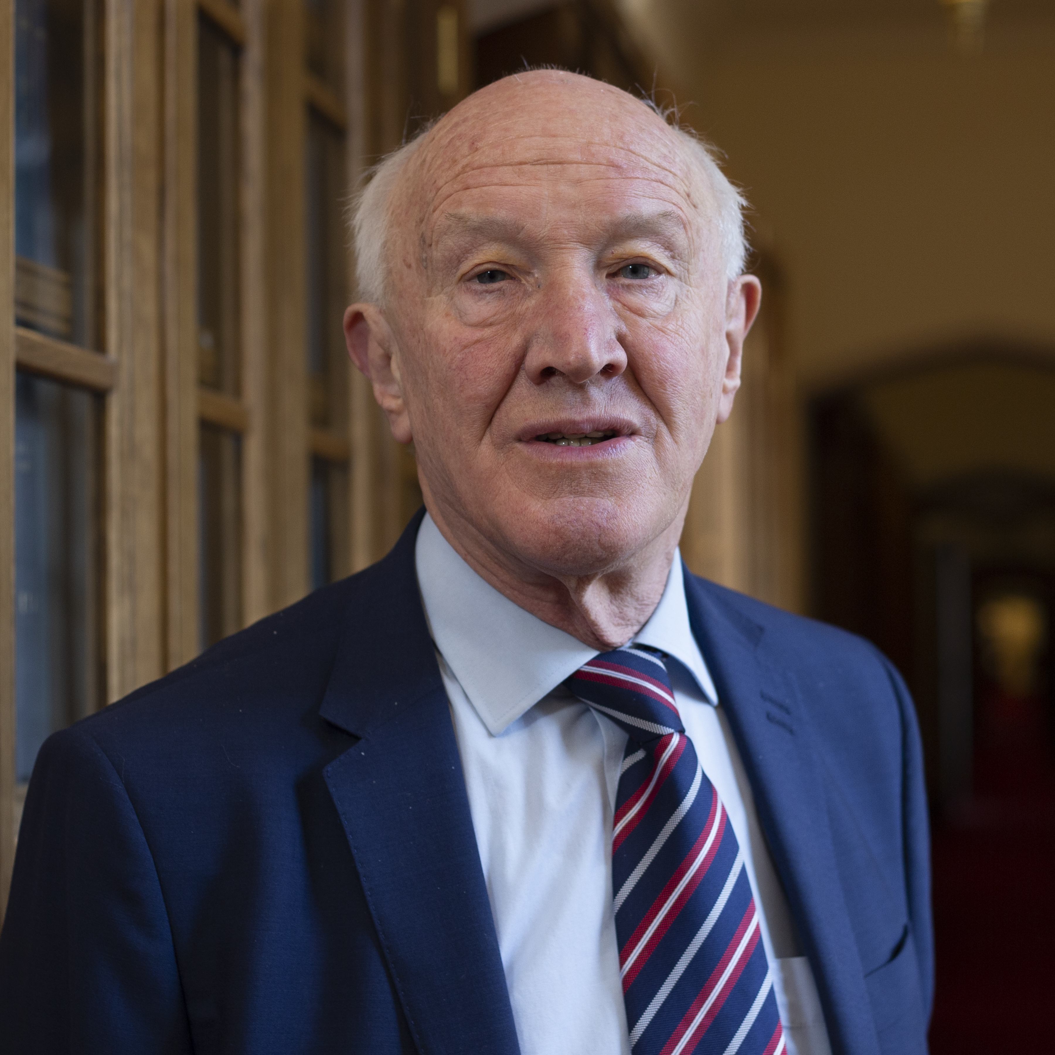 A photograph of the bust and head of David Clark who is wearing a blue suit with a blue, white, and red tie. 
