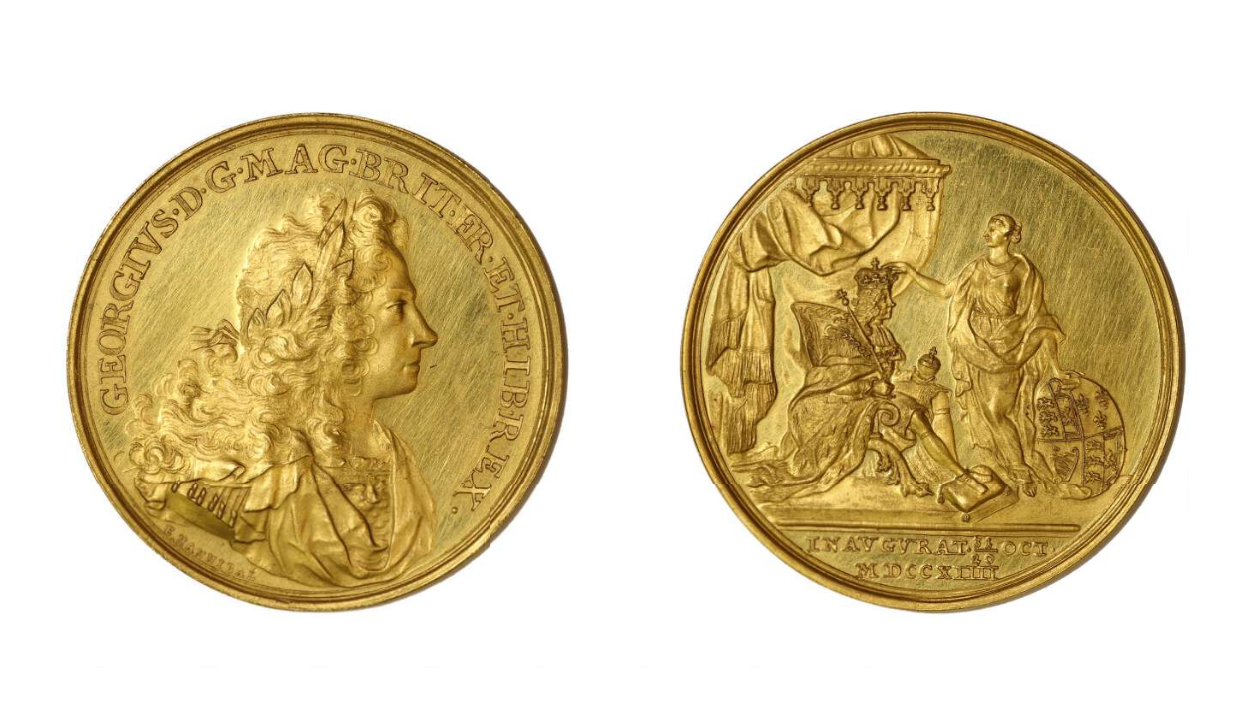 Two sides of the same gold medal. One has an image of the side profile a man with long flowing hair. One side has an image of a king being crowned on a throne, next to him is a person holding a shield.