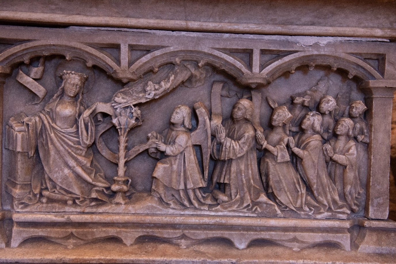 A panel on a tomb with multiple figures on the left is a woman and on the right are multiple people knelt. 