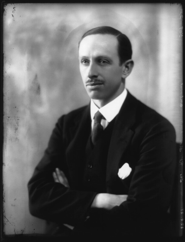 A whole-plate glass negative of a white man with short dark hair and a moustache. He is wearing a three piece suit with a tie. He is sat down with his arms crossed. 