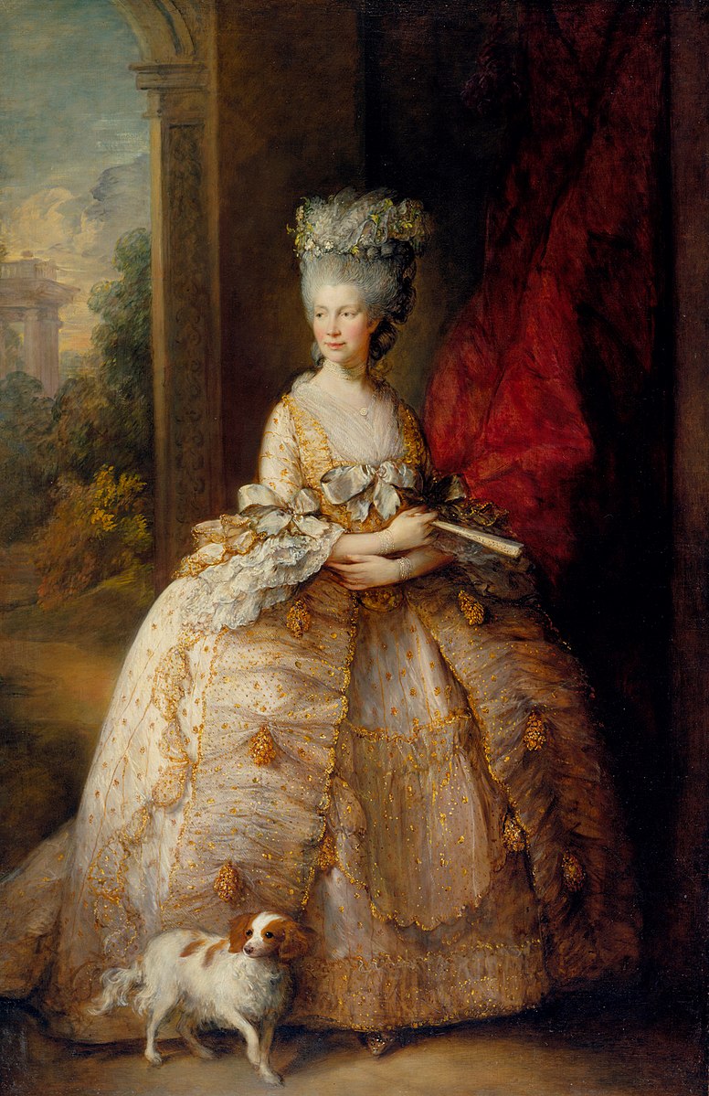 Painting of a woman in a large white gown with gold frills and detailing. There is a bow on the front of her gown and large ruffles on her sleeves. She has grey hair piled high on top of her head and floral details woven into it. She is looking to the side and has her hands crossed across her stomach. There is a fan in her right hand and a small white and brown dog by her feet.