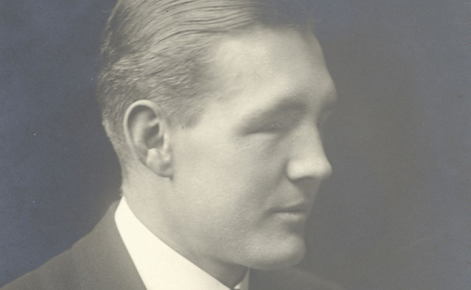 A black and white photograph of the right side of a white mans face. His hair is short and slicked back. He is wearing a suit.