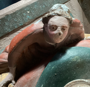 A photograph of an angel on an effigy. Her face has been worn down and her nose and mouth have been flattened. Her eyes are very prominent which is quite disconcerting. 