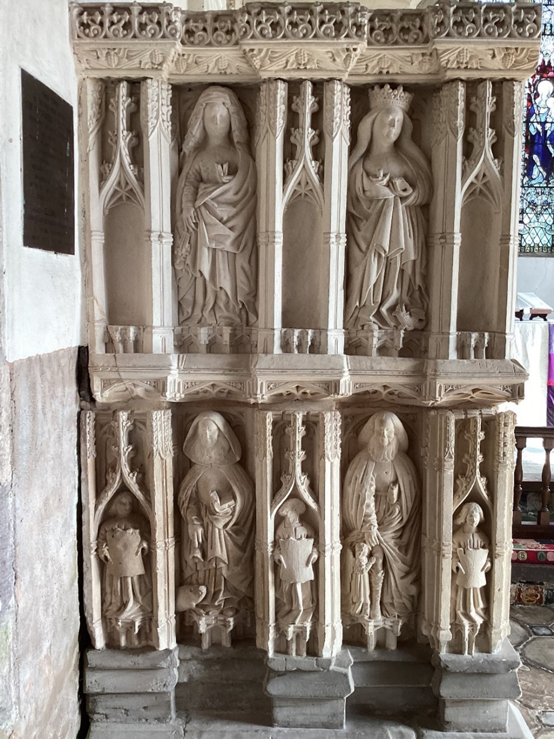 A photograph of the head of a tomb that has been carved. On the top are two figures of saints, and on the bottom are two figures of saints separated by smaller carvings of figures.