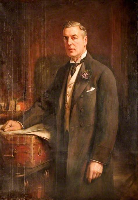 Portrait of Joseph Chamberlain. He is stood with his right arm resting on a red dispatch box on a table. He has short hair combed back from a side parting and is wearing a monocle. He wears a white shirt and patterned tie, with a cream waistcoat and a black double breasted formal jacket. A light pink orchid is pinned to his lapel.