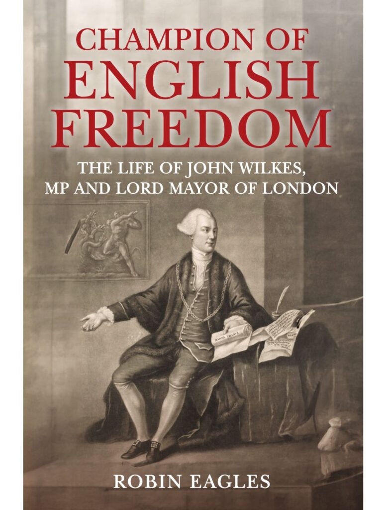 Picture of a book cover, with the title 'Champion of English Freedom' in capital letters and red font. In a smaller font and white writing is the subtitle 'the Life of John Wilkes, MP and Lord Mayor of London'. At the bottom of the page, in the same size white font is the author's name, Robin Eagles. the main image is a drawing of a man sat at a chair, with various papers displayed in front of him.