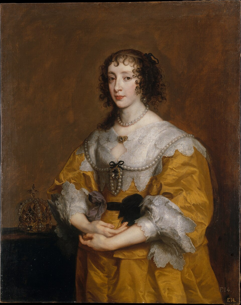 Colour portrait of Queen Henrietta Maria by Anthony Van Dyck. Queen Henrietta Maria is wearing a gold dress, with white lace collars and sleaves. She is wearing two large pearl necklaces of varying lengths. Her hands are clasped together and she has dark curly hair. Beside her is a crown on a table. 